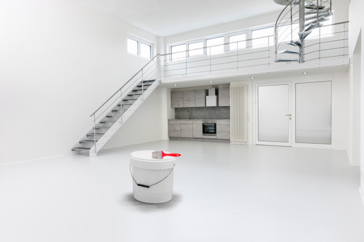 ein Kübel mit weißer Farbe steht in einem weiß ausgemalten großen leeren Wohnraum